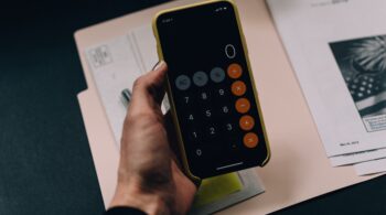 A hand of a woman of colour, holding a phone with the calculator app open, budgeting