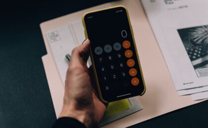 A hand of a woman of colour, holding a phone with the calculator app open, budgeting
