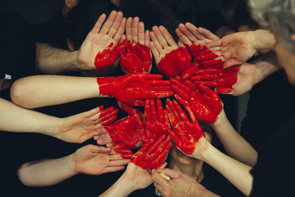 Women and men's hands form together with a heart painted in red in their palms.