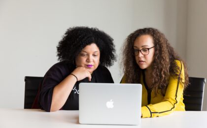 Two Black women looking at the screen of a personal computer, while securing their banking accounts.
