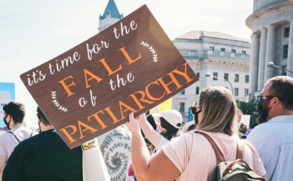 Woman holding a cardboard sign in a march that says 'It's Time for the Fall of the Patriarchy'